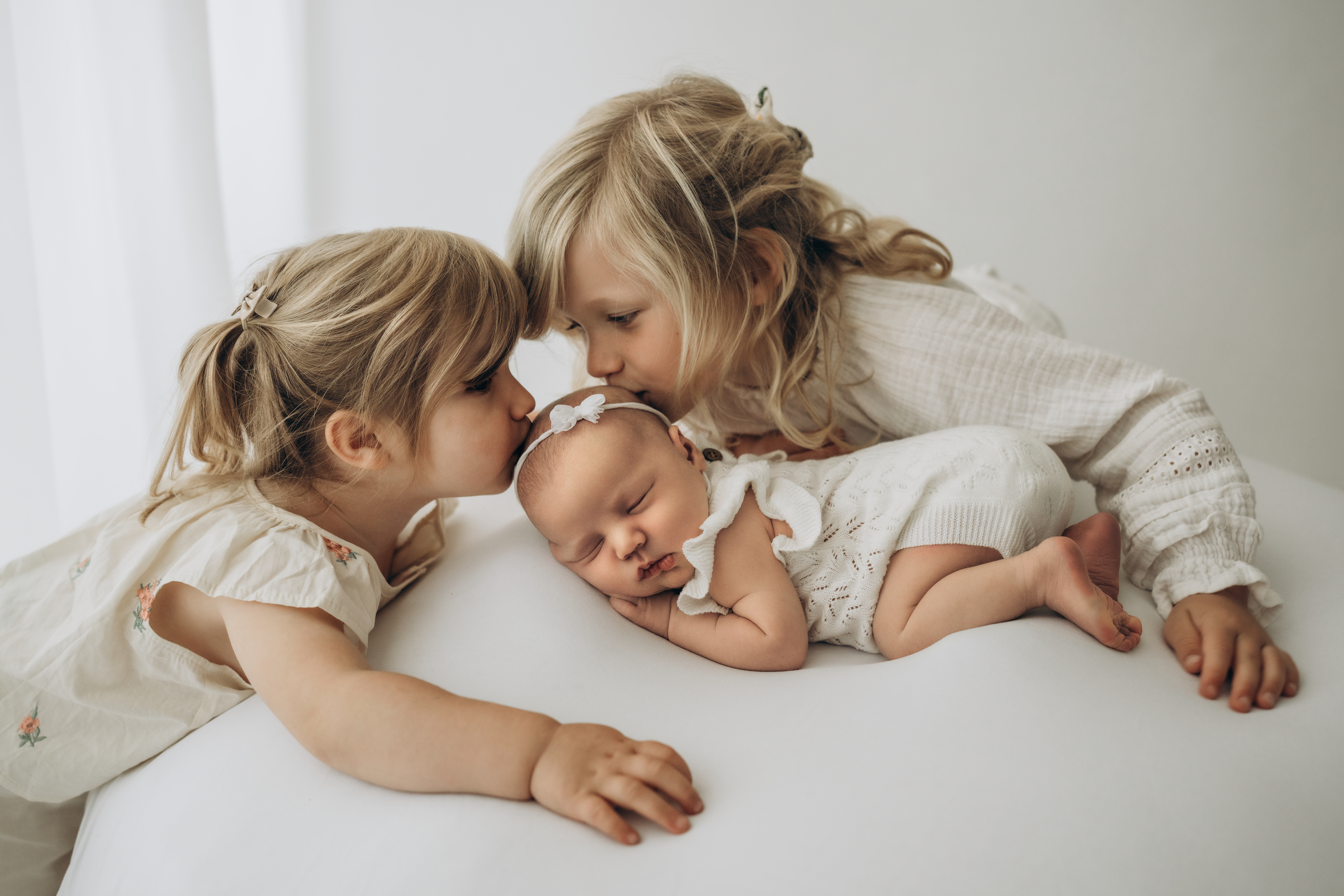 Große Schwestern küssen kleine Baby Schwester auf den Kopf